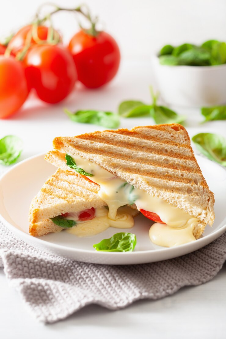 Foto sándwich de queso y tomate a la parrilla sobre fondo blanco.