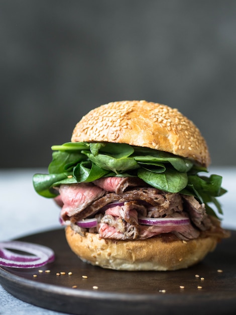 sandwich con rodajas de filete, salsa de salsa, espinacas y cebolla roja. Hamburguesa de pan con sésamo y bistec.