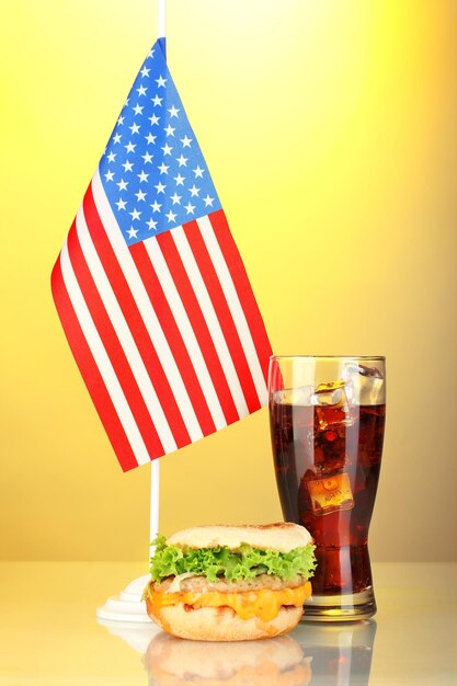 Sándwich sabroso y cola con bandera americana sobre fondo amarillo