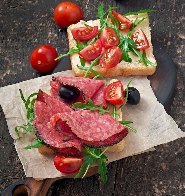 Sandwich con salchichas, aceitunas, tomate y rúcula sobre la vieja mesa de madera