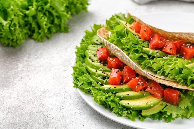 Sándwich con salmón, aguacate, lechuga, semillas de sésamo, tortilla de pan plano sobre fondo gris, refrigerio simple