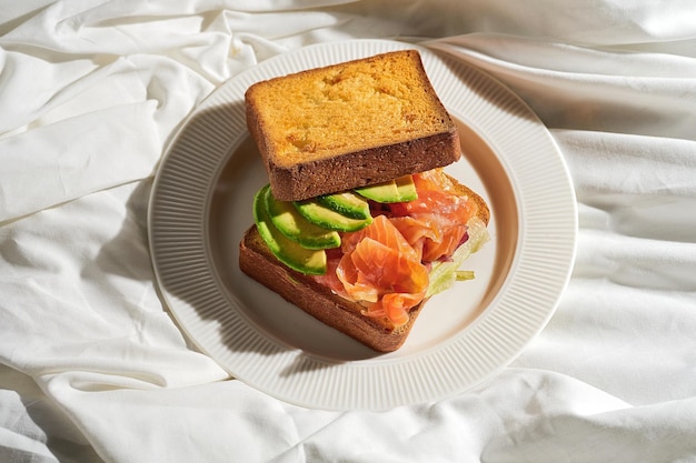 Sándwich de salmón y aguacate tostado en un plato sobre una sábana blanca Luz dura