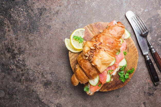 Sándwich de salmón ahumado con queso crema fresco y pepinos en la tabla de cortar, vista superior