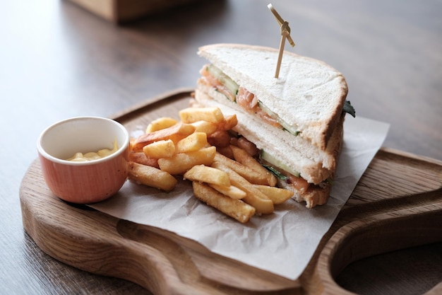 Sándwich de salmón y pepino con salsa de queso y papas fritas en una tabla de madera en un café Almuerzo de negocios o brunch Fotografía horizontal Enfoque selectivo