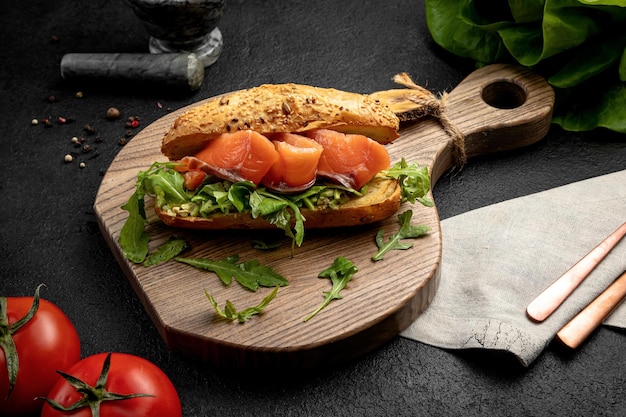 Sándwich con salmón y rúcula servido en una tabla de madera sobre un fondo oscuro