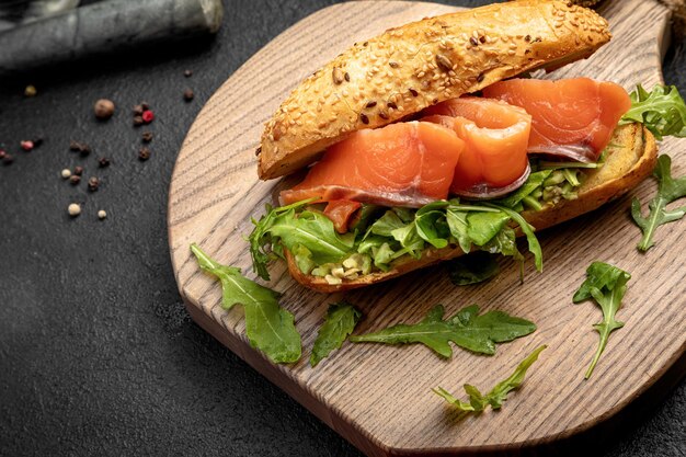 Sándwich con salmón y rúcula servido en una tabla de madera sobre un fondo oscuro