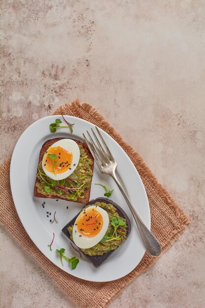 Sándwich saludable con aguacate, huevos y microgreens sobre tostadas en un plato para el desayuno. Concepto dietético de nutrición saludable. Vista superior.