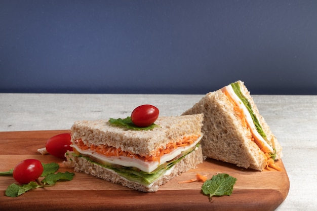Foto sándwich saludable en lonchas de pan integral relleno de zanahoria, lechuga, mozzarella y jamón.