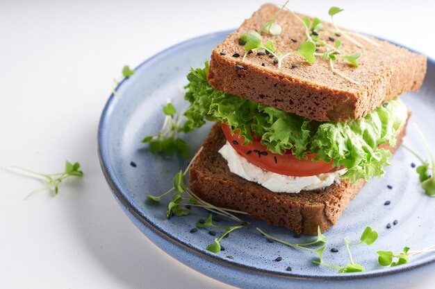 Sándwich saludable con pan sin gluten, tomate, lechuga y microgreens germinados, espolvoreado con semillas de sésamo servido en plato