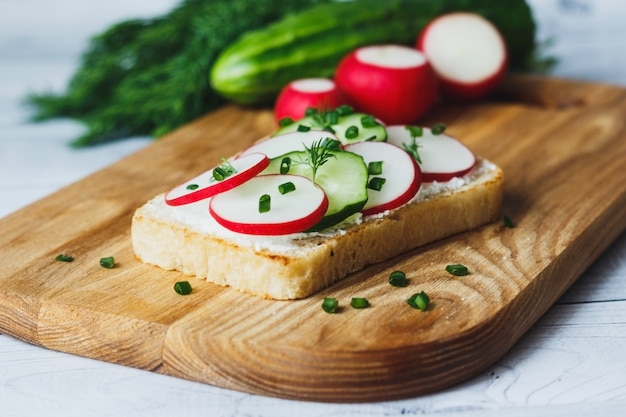 Sándwich saludable con pepino de rábano y queso crema sobre tabla de cortar de madera