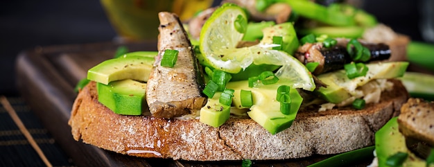 Sandwich - smorrebrod mit Sprotten-, Avocado- und Frischkäse auf hölzernem Brett.