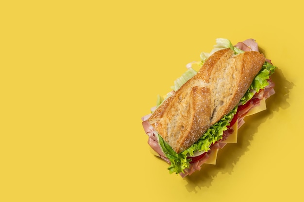 Sándwich submarino con jamón, queso, lechuga, tomate, cebolla, mortadela y salchicha sobre fondo amarillo