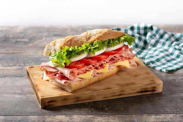 Sándwich submarino con jamón, queso, lechuga, tomate, cebolla, mortadela y salchicha sobre mesa de madera