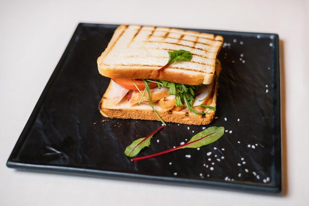 Sándwich con tomate de jamón y hierbas en plato cuadrado negro Proceso de cocción de alimentos