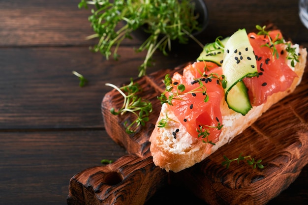 Sándwich Tostadas de salmón con queso crema pepino sésamo negro y microgreens sobre fondo de mesa de madera vieja Mariscos Comida saludable Fotografía en clave baja Vista superior