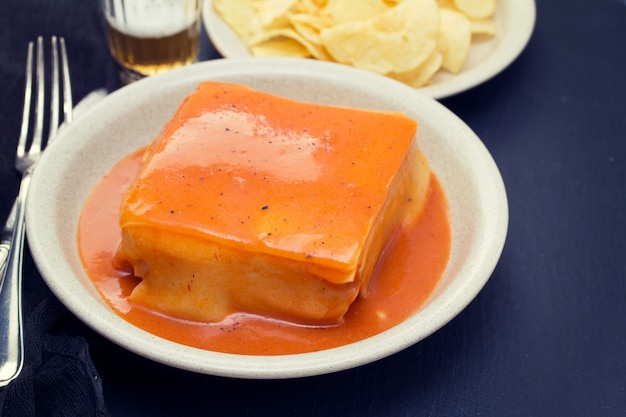 Sándwich tradicional portugués con salsa francesinha en plato