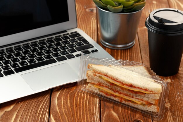 Sándwich de triángulo en la mesa de oficina de madera con laptop y taza de café