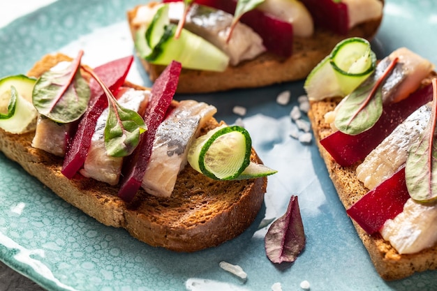 Sándwich con trozos de filete de arenque marinado Ensalada de remolacha cebolla verde pepino y microgreen Tostada con filete de arenque Cocina escandinava