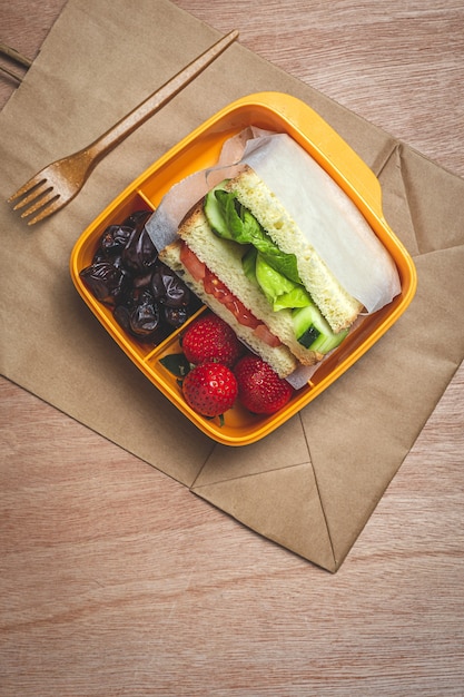 Sandwich vegano en recipiente de plástico sobre mesa de madera. Concepto de comida sana