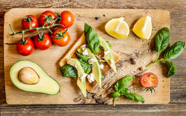 Sándwich con verduras y limón, tomates cherry, aguacate, hojas de limón en una vista superior de la tabla de madera