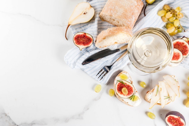 Sandwiche mit Ricotta- oder Frischkäse, Ciabatta, frischen Feigen, Birnen, Traube, Walnüssen und Honig auf weißer Marmortabellentabelle, mit Draufsicht des Weinglases