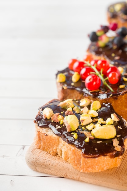 Sandwiche mit schokoladenmasse, pistazien und frischen beeren auf einem hölzernen umhüllungsbrett.