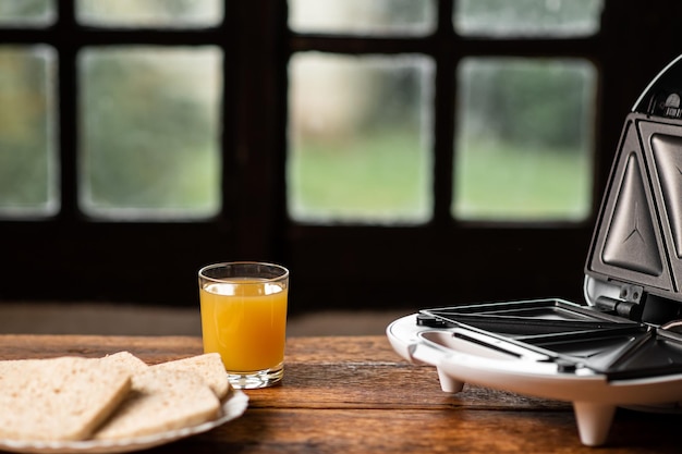 Sandwichera y un vaso de jugo en el fondo de una ventana antigua Preparando un refrigerio rápido para el desayuno por la mañana