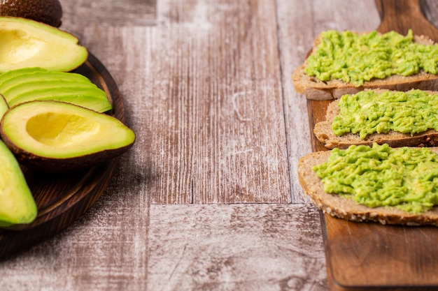 Sándwiches de aguacate junto a los cortados sobre tabla de madera.