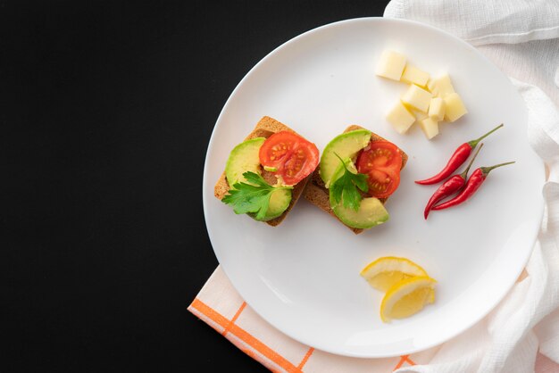 Sándwiches con aguacate orgánico fresco y tomate rojo en superficie negra, desayuno vegano