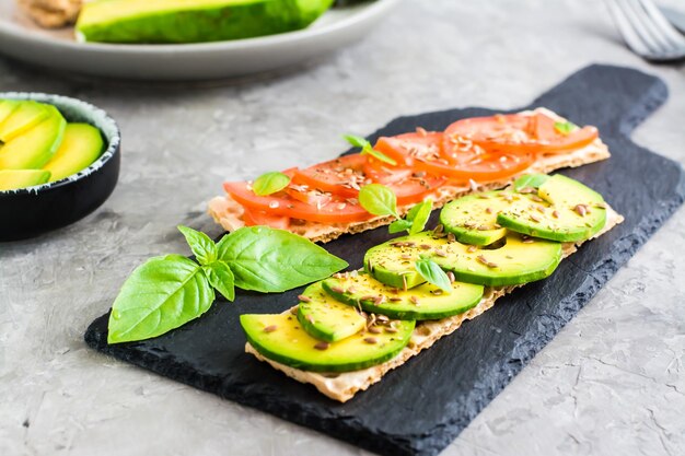 Sándwiches apetitosos con aguacate y tomates en pan de grano en pizarra en la mesa Comida vegetariana saludable