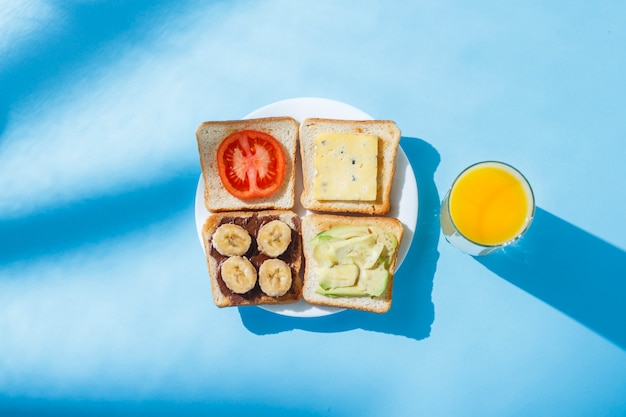 Sandwiches auf einem weißen Teller, ein Glas mit Orangensaft, eine blaue Oberfläche. Flachgelegt, Draufsicht.