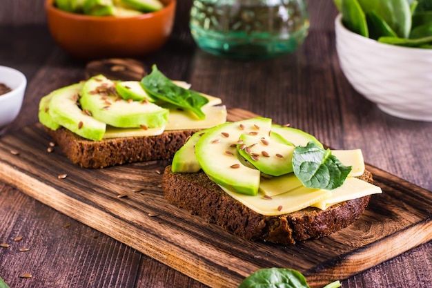 Sandwiches auf Roggenbrot mit Käse, Avocado, Spinat und Leinsamen auf einem Holzbrett auf dem Tisch