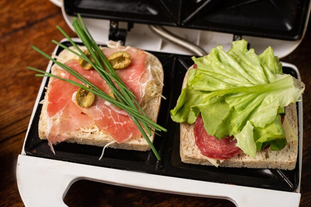 Sandwiches aus Schinkengemüse und Käse in einem Sandwichmaker zubereiten Zwei Toasts mit unterschiedlichen Füllungen in der Nähe