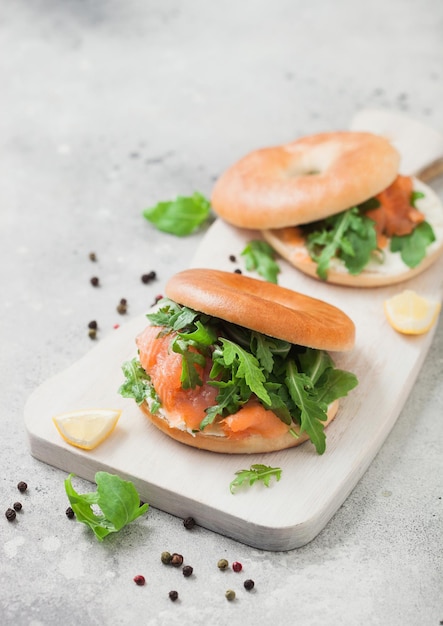 Sándwiches de bagel y salmón con queso crema y rúcula salvaje y limón con pimienta sobre fondo de cocina claro