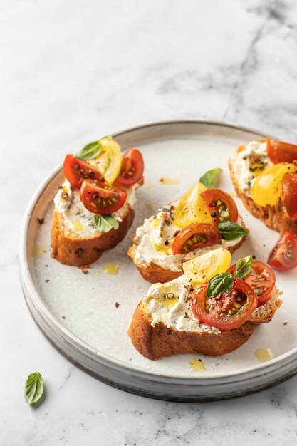 Foto sándwiches de bruschetta con tomates, queso crema, aceite de oliva y albahaca en un plato de mármol blanco