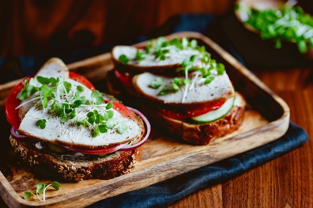 Sándwiches con carne de pavo y verduras frescas servidos con microvegetales en un plato de madera