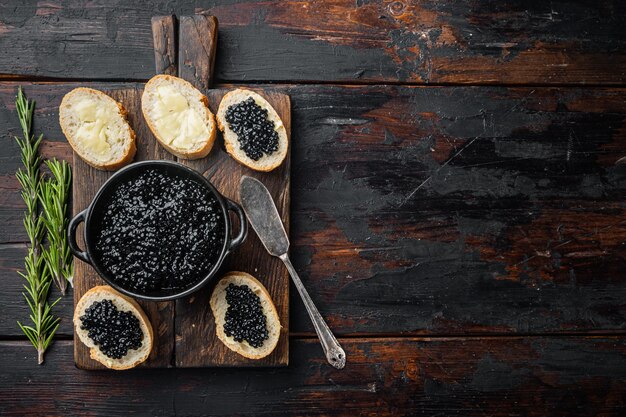 Sándwiches con caviar negro, en la vieja mesa de madera oscura, vista superior plana