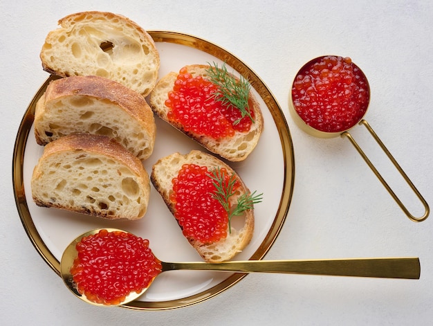 Sándwiches con caviar rojo y pan en un plato redondo en una mesa blanca