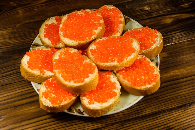 Sándwiches con caviar rojo sobre mesa de madera rústica. Vista superior