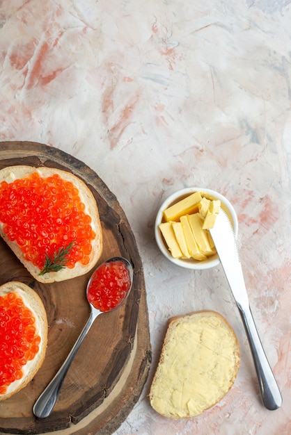 Sándwiches de caviar de vista superior con cubiertos y queso sobre una tabla de cortar sobre una superficie ligera