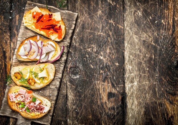 Sándwiches con champiñones, salami, caviar rojo y verduras frescas sobre pan tostado en la mesa de madera.