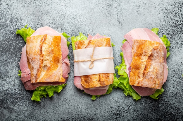 Sándwiches de chapata fresca con jamón, queso, lechuga sobre fondo de hormigón de piedra, primer plano, vista superior. Hacer sándwiches saludables para el concepto de merienda o almuerzo