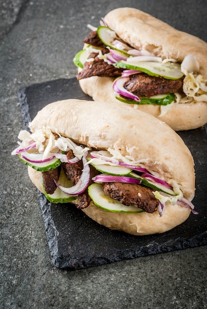 Sandwiches Comida rápida. Chino tradicional asiático bao bollos con carne rellena de cerdo, ternera, verduras frescas y salsa picante. Sobre una mesa de piedra oscura.