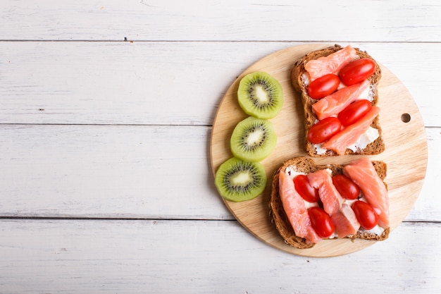 Sandwiches des geräucherten Lachses mit Butter- und Kirschtomaten auf weißem hölzernem Hintergrund.