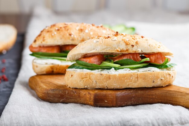 Sandwiches des geräucherten Lachses mit Gurke und Spinat auf hölzernem Brett auf einem Leinenhintergrund.