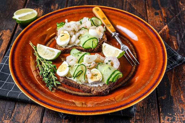 Sándwiches escandinavos con camarones, gambas, huevos de codorniz y pepino sobre pan de centeno. Fondo de madera oscura. vista superior.