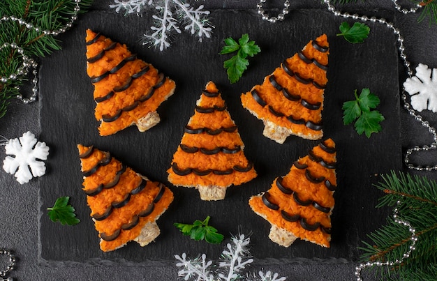 Sándwiches en forma de árbol de navidad de queso de zanahoria y aceitunas negras en pan blanco sobre fondo gris oscuro