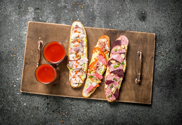 Sándwiches frescos con jugo de tomate onn bandeja antigua sobre mesa rústica.