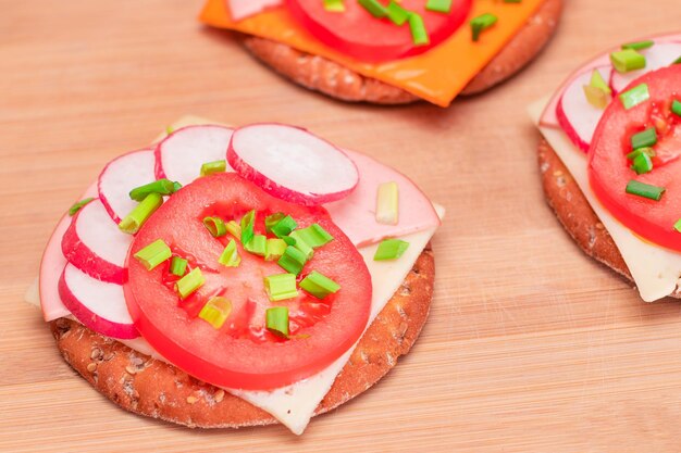 Sándwiches de galletas crujientes con salchichas de tomate, queso, cebollas verdes y rábanos