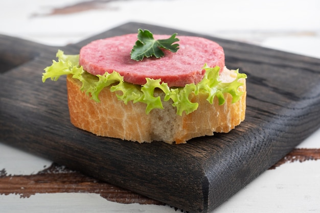 Sándwiches con hojas de lechuga y salchicha de salami en rodajas sobre una tabla de madera.